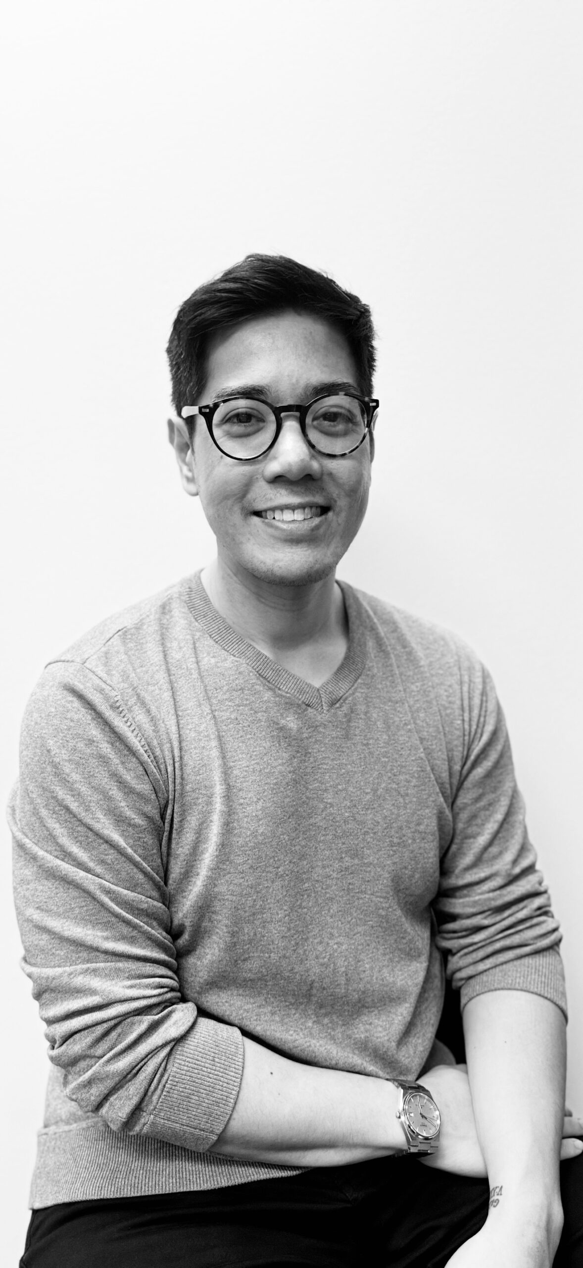 Black and white portrait of a woman with shoulder-length dark hair, wearing a white top. She has a calm and confident expression, looking directly at the camera. The background features a textured brick wall.
