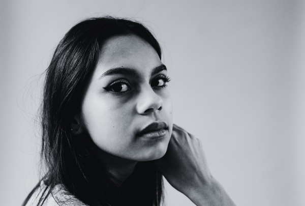A black and white image of a couple sitting closely together on a gray couch focused on a laptop screen. The woman, with long dark hair, is wearing a cozy green cardigan over a beige top and is pointing at the screen. The man, with a beard and his hair tied in a bun, is wearing a dark green cable-knit sweater and bracelets on his wrist. The room is softly lit, with a floor lamp and decorative pillows adding warmth to the space.