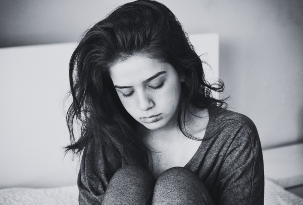 A black and white image of a couple sitting closely together on a gray couch focused on a laptop screen. The woman, with long dark hair, is wearing a cozy green cardigan over a beige top and is pointing at the screen. The man, with a beard and his hair tied in a bun, is wearing a dark green cable-knit sweater and bracelets on his wrist. The room is softly lit, with a floor lamp and decorative pillows adding warmth to the space.